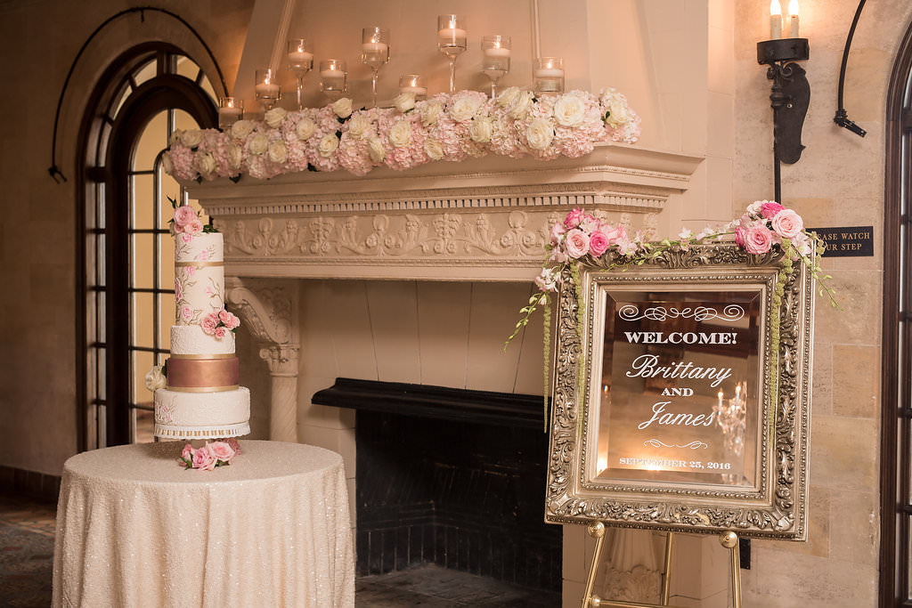 Wedding Reception Decor, Wedding Welcome Sign on Antique Gold Framed Mirror, Blush Pink and White Floral Arrangements on Fireplace with Floating Candles, Tall Four Tier White, Rose Gold, and Floral Wedding Cake | Tampa Bay Wedding Photographer Cat Pennenga Photography | Wedding Planner NK Productions | Sarasota Wedding Venue Powel Crosley Estate