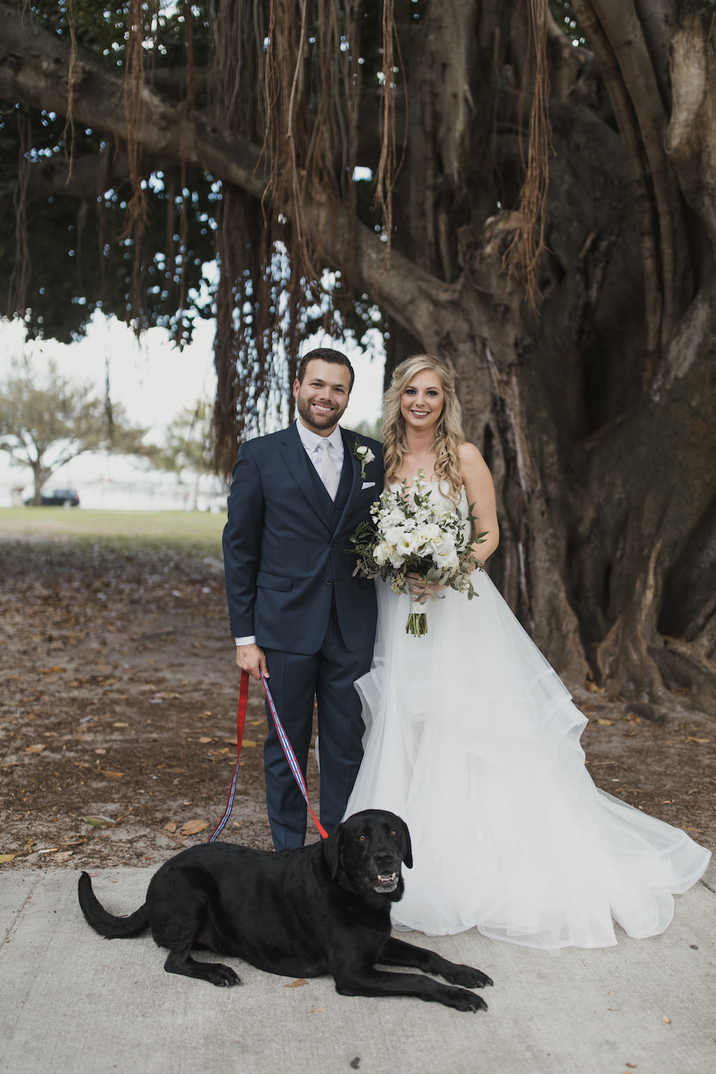 Outdoor Florida Bride and Groom Wedding Portrait, Bride in Strapless Hayley Paige Chantelle Gown, Ivory Tulle Skirt Ball Gown, Lace Corset Bodice with Greenery and Floral Garden Inspired Bouquet, Groom in Navy Blue Suit with Dog | Tampa Bay Wedding Hair and Makeup Artist Michele Renee the Studio
