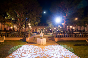 Nighttime Outdoor Garden Courtyard Wedding Reception Decor, Heart Shaped Projection, Round Table with Five Tier Wedding Cake on Gold Stand | Sarasota Wedding Venue Ringling Museum | Tampa Bay Wedding Planner NK Weddings