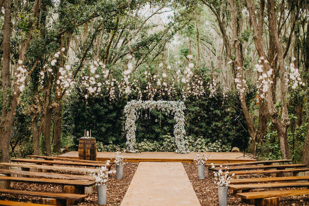 Elegant Outdoor Rustic Wedding Ceremony Decor, White and Greenery Floral Arch with Hanging Glass Bulbs | Lakeland Rustic Wedding Venue The Prairie Glenn Barn at Gable Oaks Ranch