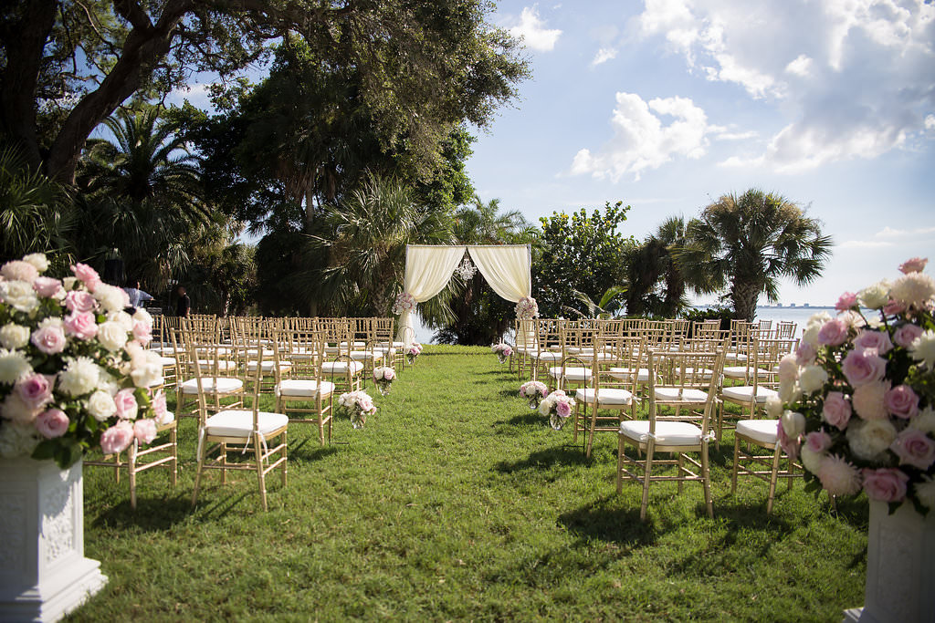 Florida Outdoor Waterfront Wedding Ceremony Decor, Arch with White Draping and Floral Bouquets, White Pedestals with Blush Pink, White and Greenery Floral Bouquets, Gold Chiavari Chairs | Tampa Bay Wedding Photographer Cat Pennenga Photography | Sarasota Wedding Planner NK Productions | Sarasota Wedding Venue Powel Crosley Estate