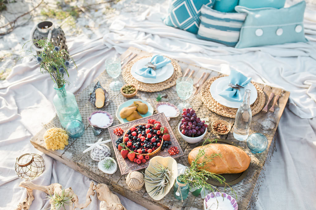 Florida Beach Inspired Wedding Styled Shoot, Wood Plank, Blue Decorative Pillows, Natural Jute Braided Charger, White China Dishes, Light Blue Linens, Seashell Place Cards, Rose Gold Silverware, Fruit Platters and Aqua Crystal Glasses with Fishing Net Table Runner | Tampa Bay Wedding Planner UNIQUE Weddings and Events | Rentals Over the Top Linen Rentals