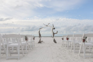 Florida Beachfront Wedding Ceremony Decor, White Folding Chairs with Geometric Vase and Red and Green Florals, Birchwood Arch with White Drapery | Tampa Bay Wedding Photographer Lifelong Photography Studios | Hotel Wedding Venue Hilton Clearwater Beach