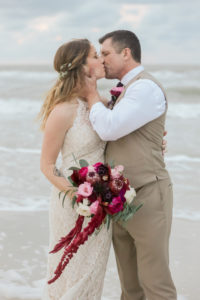 Florida Bride and Groom Sunset Wedding Portrait on the Beach, Bride in Long Fitted Lace Halter Strap BHLDN Wedding Dress with Jewel Tone, Purple, Pink, Plum, White and Greenery Organic Floral Bouquet, Groom in Khaki Suit and Vest | Tampa Bay Wedding Photographer Lifelong Photography Studios | Clearwater Beach Hotel WEdding Venue Hilton Clearwater Beach | Hair and Makeup Artist Femme Akoi