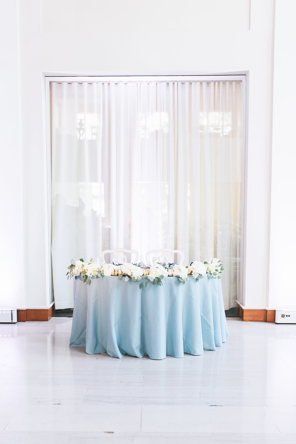 Elegant, Classic Wedding Reception Decor, Sweetheart Table with Dusty Blue Tablecloth, White and Greenery Florals with White Draping Background | Downtown Tampa Wedding Venue The Vault