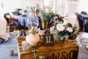 Vintage Rustic Whimsical Inspired Wedding Reception Decor, Round Table with Dusty Blue Tablecloth, Gold Chargers, Navy Blue Linens, Wooden Pallet Box with Candelsticks, Vases with Greenery and White Floral Centerpieces | Tampa Bay Wedding Planner Love Lee Lane