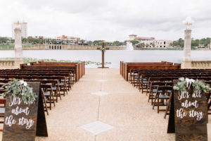 Tampa Bay Lakefront Wedding Ceremony Decor, Wooden Folding Chairs, Custom Folding Wooden Signs with Greenery Garland, Wooden Cross | Lakeland Wedding Venue Lake Mirror Amphitheater | Wedding Planner Love Lee Lane | Rentals A Chair Affair