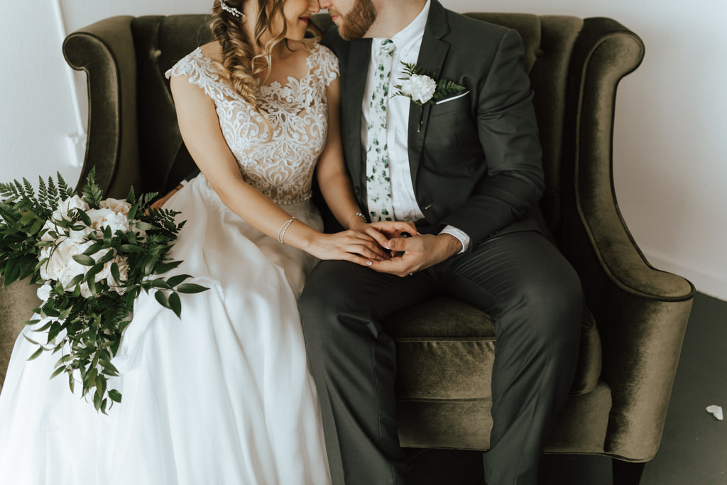 Tampa Bay Bride and Groom Wedding Portrait on Dark Green Velvet Loveseat, Bride in Nude/Ivory Lace Off the Shoulder Bodice, Flowy White Skirt, Organic Ivory and Greenery Floral Bouquet | Lakeland Wedding Venue HAUS 820