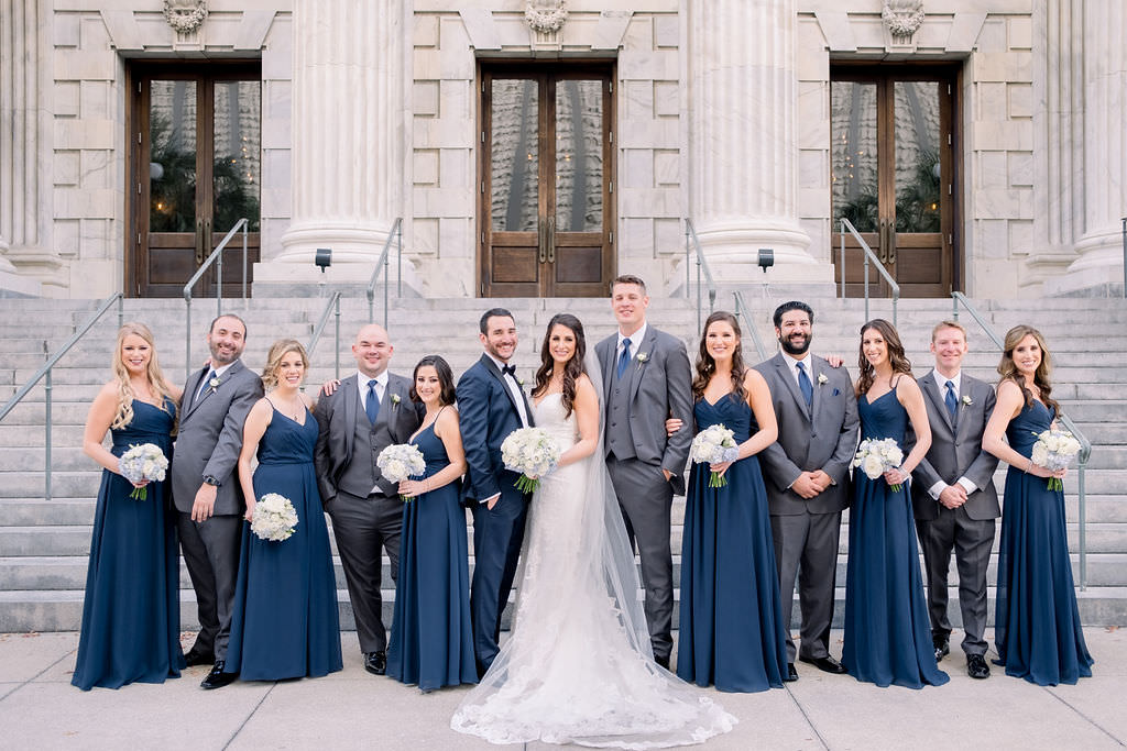 Florida Bride, Groom, Bridesmaids, Groomsmen at Downtown Tampa Hotel Venue Le Meridien, Bridesmaids in Matching Navy Blue Dresses, Groomsmen in Grey Suits with Blue Ties, Groom in Navy Blue and Black Tuxedo, Bride in Strapless Sweetheart Lace Fitted Wedding Dress with Cathedral Length Veil