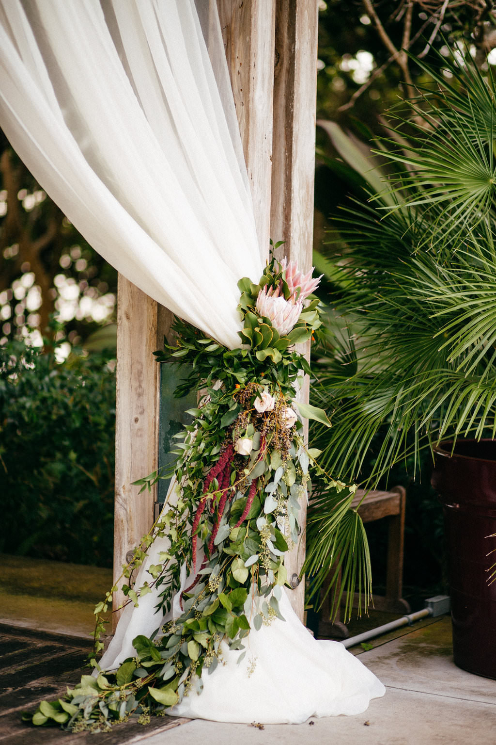 Garden Inspired Wedding Ceremony Decor, White Drapery, Greenery Garland, Red Hanging Amaranthus King Protea Flowers | Tampa Bay Wedding Planner NK Weddings