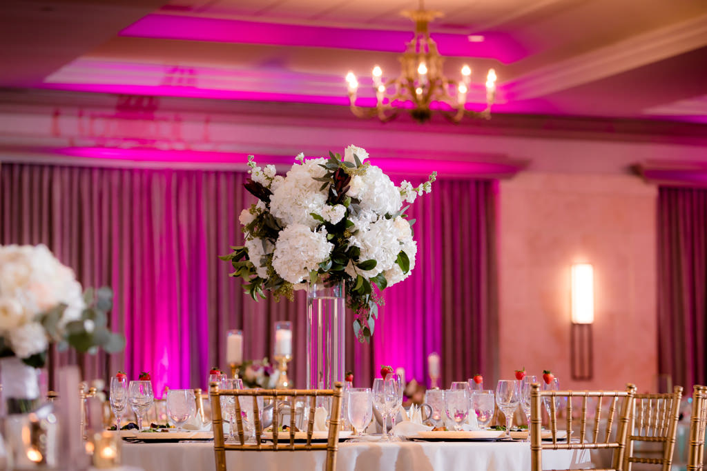 Hotel Ballroom Classic Wedding Reception Decor, Pink Uplighting, Round Tables with Gold Chiavari Chairs, White Tablecloth, Tall Glass Cylinder Vase with White and Greenery Floral Centerpiece | Wedding Planner Special Moments Event Planning | Rentals Gabro Event Services | Tampa Marriott Water Street