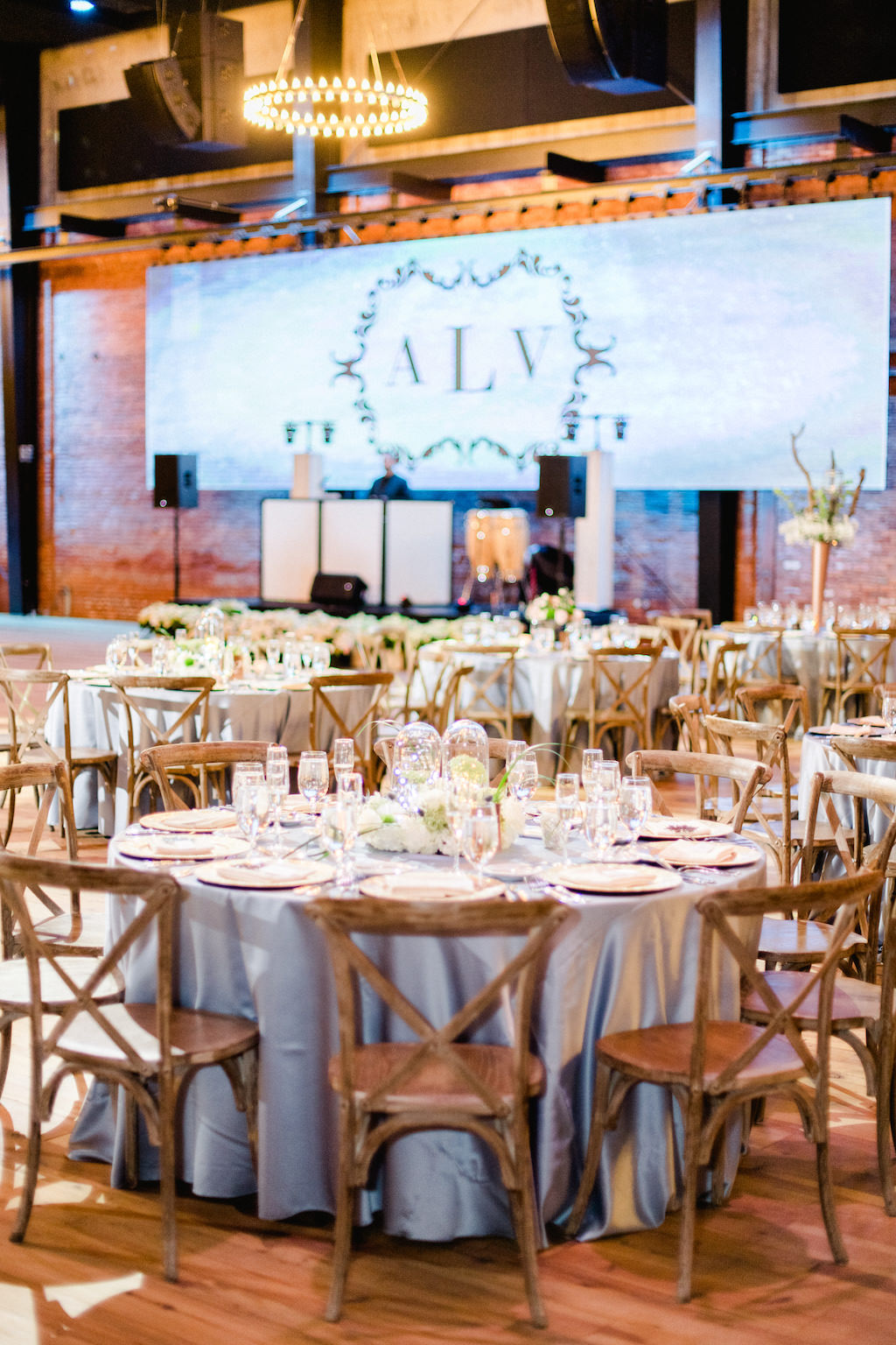 Wedding Reception Deco, Round Tables with Dusty Blue Tablecloths, Wooden Chiavari Chairs, Projector Screen with Monogram Initials | Historic Industrial Tampa Bay Wedding Venue Armature Works