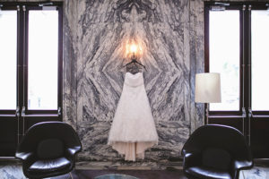 Strapless Lace Ballgown Wedding Dress with Rhinestone Belt Hanging in Front of Black and White Marble Wall