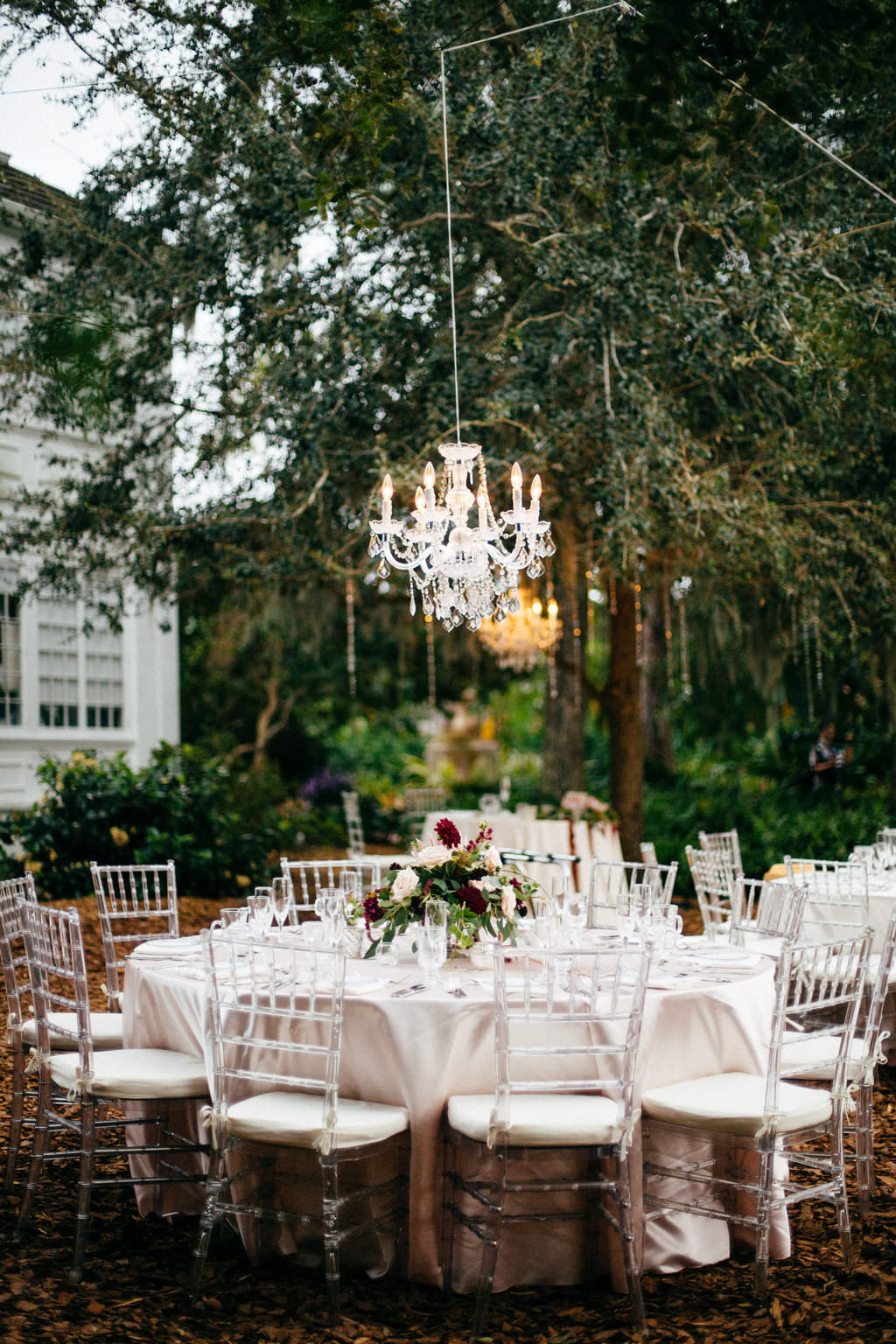 Outdoor Garden Wedding Reception Decor, Round Tables with Ivory Tablecloths, Ghost Acrylic Chiavari Chairs, Low Flower Centerpiece, Hanging Crystal Chandelier | Sarasota Wedding Venue Marie Selby Botanical Gardens | Tampa Bay Wedding Planner NK Productions