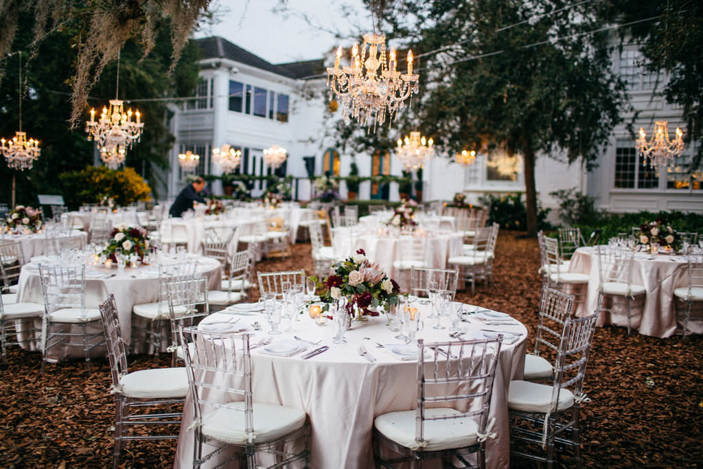 Outdoor Garden Wedding Reception Decor, Round Tables with Ivory Tablecloths, Ghost Acrylic Chiavari Chairs, Low Flower Centerpiece, Hanging Crystal Chandelier | Sarasota Wedding Venue Marie Selby Botanical Gardens | Tampa Bay Wedding Planner NK Productions