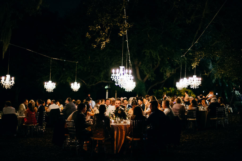 Nighttime Wedding Reception Dinner Portrait Under Hanging Crystal Chandeliers | Tampa Bay Wedding Planner NK Productions | Sarasota Wedding Venue Marie Selby Botanical Gardens