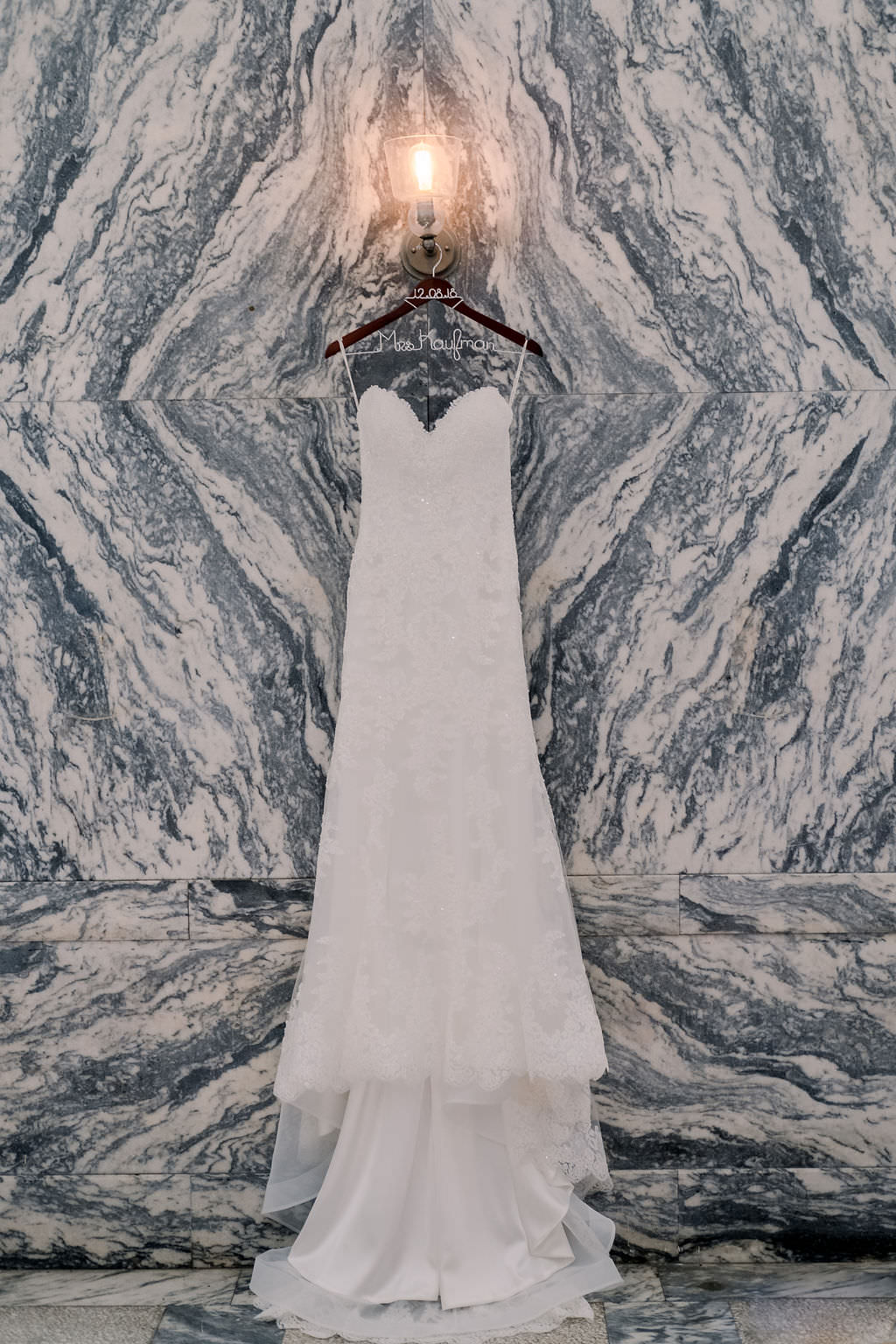 Strapless Sweetheart Lace Fitted Maggie Sottero Wedding Dress on Custom Hanger and Marble Wall Backdrop