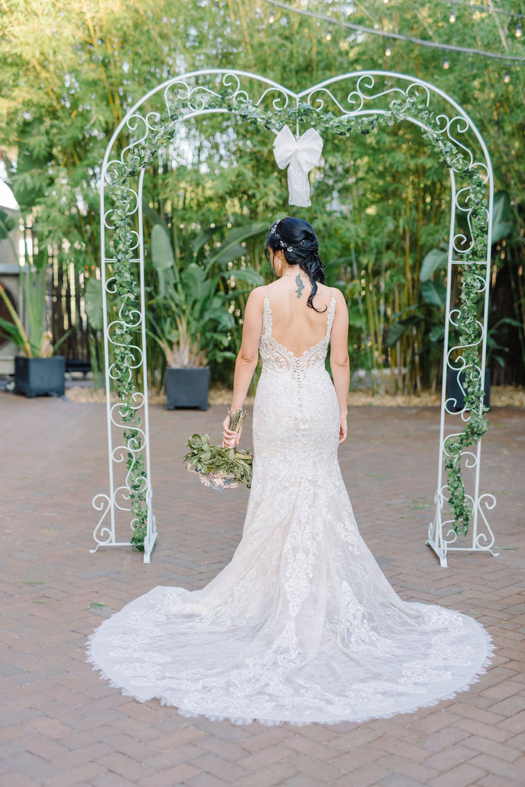 Bride in lace wedding dress under metal and greenery arch