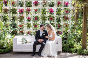 Romantic Bride and Groom Sarasota Garden Wedding Portrait on White Couch with Tropical Flowers and Greenery Backdrop | Sarasota Wedding Venue Marie Selby Botanical Gardens