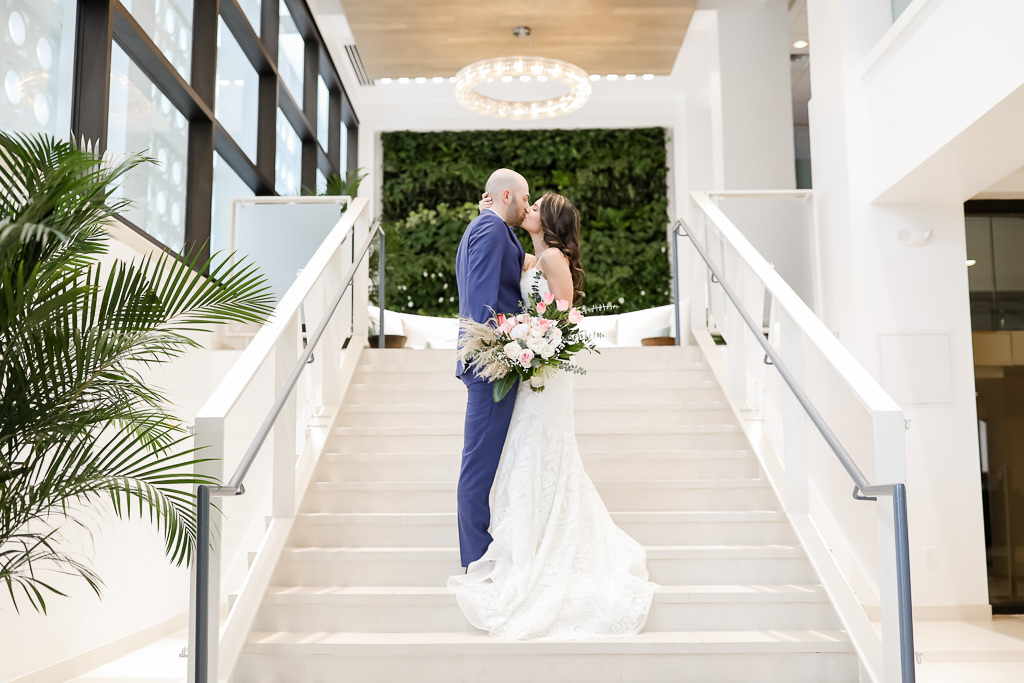 Florida Bride and Groom Intimate Wedding Portrait on Hotel Staircase in Courtyard, Groom in Blue Tuxedo, Bride in White and Pink Flower Bouquet with Green Palms, Bride in Spaghetti Strap White Fitted Hayley Paige Wedding Dress | Photographer Lifelong Photography Studios | Hotel Wedding Venue The Hilton Clearwater Beach Resort & Spa