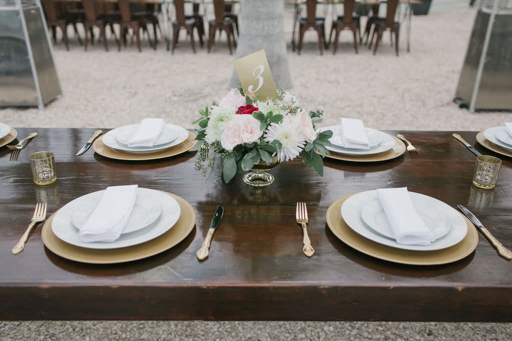 Open Air St. Pete Wedding Reception with Farm Tables with Gold Charger Plates and Vintage Tabletop Decor Accents in a Gold Cauldron with Ivory and Pink Florals and Greenery | Outdoor St. Pete Wedding Reception Venue Intermezzo