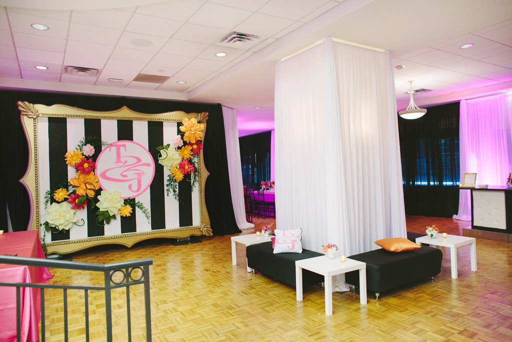 Whimsical Kate Spade Inspired Wedding Reception Decor, Seating Lounge Area with Black Benches, White Side Tables, White Linen Drapery, Large Gold Frame with Black and White Stripes, Pink Monogram and Colorful Paper Flowers, Pink Uplighting | Tampa Bay Wedding Planner Parties A LA Carte
