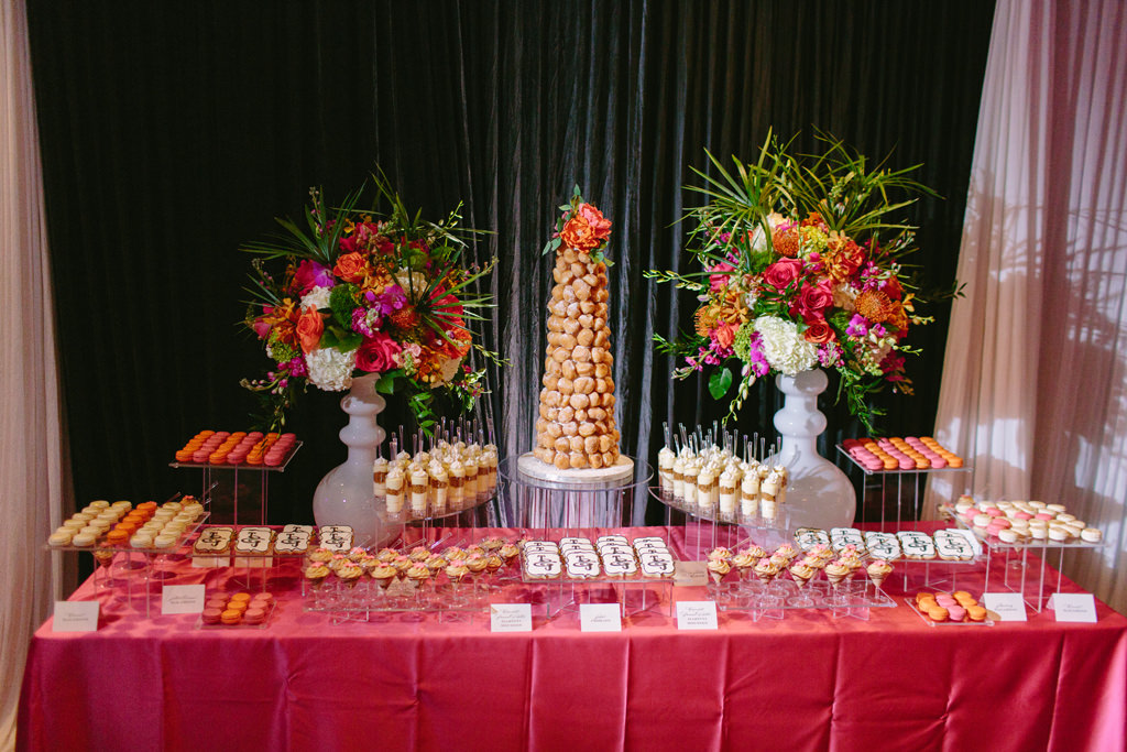 Whimsical Kate Spade Wedding Reception Decor, Dessert Table with Hot Pink Tablecloth, Tall White Vases with Colorful Orange, Pink, Purple, White, and Green Flower Centerpiece, Donut Tower on Acrylic Cake Stand, Macaroons, Cookies, and Mini Desserts | Tampa Bay Wedding Planner Parties A La Carte