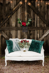 Rustic Christmas Inspired Wedding Decor, Wooden Barn Backdrop with White Vintage Loveseat with Green Pillows and Wedding Veil, Wedding Bouquet with Red Florals and Greenery, Hanging Gold Floral Hoop with Red Roses | Bushnell Florida