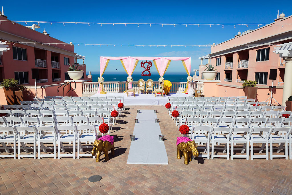 Florida Indian Hindu Rooftop Wedding Ceremony Decor, Gold Elephant Statues, White Folding Chairs, Red Floral Pom Poms, Pink and Gold Linen Drapery Arch, White Aisle Runner and String Lights | Clearwater Beach Waterfront Wedding Venue Hyatt Regency Clearwater