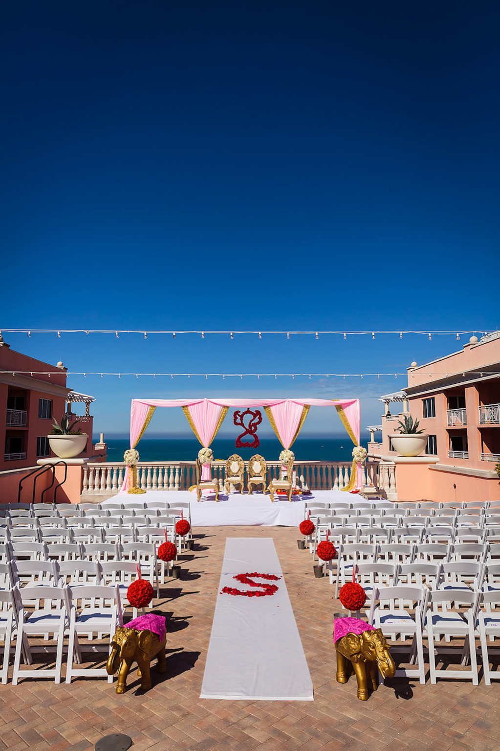 Florida Indian Hindu Rooftop Wedding Ceremony Decor, Gold Elephant Statues, White Folding Chairs, Red Floral Pom Poms, Pink and Gold Linen Drapery Arch, White Aisle Runner with Personalized Red Rose Petals and String Lights | Clearwater Beach Waterfront Wedding Venue Hyatt Regency Clearwater