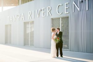 Romantic Florida Bride and Groom In Front of Tampa River Center Wedding Venue , Bride in Ivory and Gold Sheath Style Wedding Dress and Groom in Elegant Emerald Velvet Jacket, Carrying Eclectic Colorful Mix Flower Bouquet | Tampa Bay Wedding Photographer Andi Diamond Photography| Tampa Bay Wedding Makeup Artist Michelle Renee the Studio