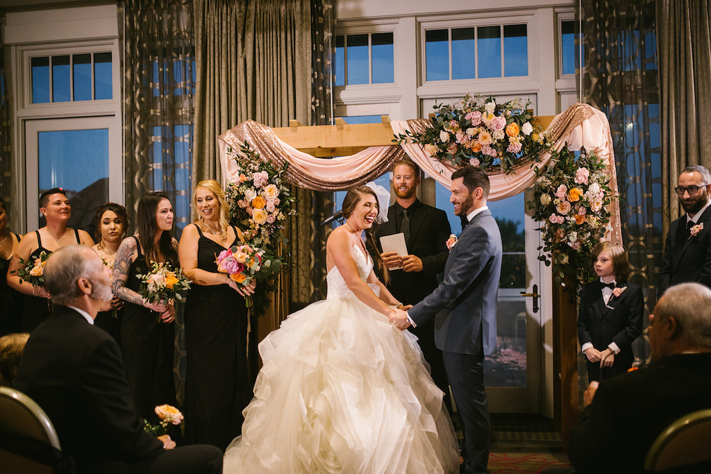 Tampa Bay Bride and Groom Exchanging Vows Under Wooden Arch with Blush Pink and Sparkle Draping and Colorful Flower Bouquets Indoor Ballroom Wedding Ceremony Portrait | Downtown St. Pete Hotel Wedding Venue The Birchwood