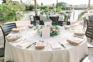 Rustic Elegant Waterfront Wedding Reception Decor, Round Tables with Ivory White Tablecloths, Black Chairs, Gold and White Table Number Sign, White Lantern with Floral and Greenery Wreath Centerpiece | Clearwater Beach Wedding Venue Island Way Grill | Wedding Planner Gulf Beach Weddings