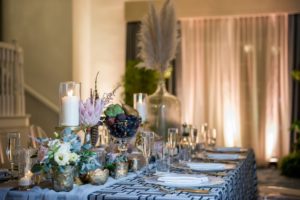 Bohemian Chic Inspired Wedding Decor, Long Rectangle Reception Tables with Blue Geometric Linen and White Sheer Runner, Neutral Tones Low Floral Centerpieces with White Ivory and Pink Roses, King Protea, Thistle, Lisianthus, Antlers, Feathers, Scabiosa, Mercury Glass Votive Candle Holder, Crystal Champagne Flutes, Pampas Grass in Large Clear Glass Jar, Against Hotel Ballroom Backdrop with Greenery and Chandelier Lighting | Tampa Bay Wedding Photographer Andi Diamond Photography | St. Pete Beach Wedding Venue The Don Cesar | Planner UNIQUE Weddings + Events | Over the Top Linens | Rentals A Chair Affair