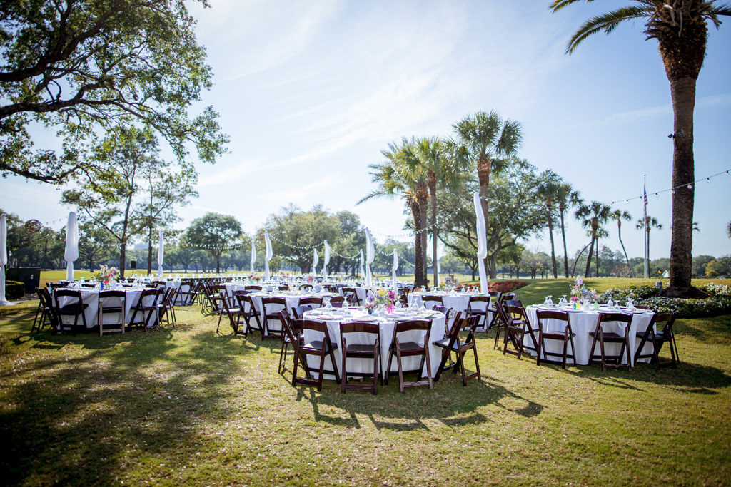 Southern Chic Wedding Decor in Outdoor Reception in South Tampa, White Round Tables with Wooden Folding Chairs, Colorful Centerpieces, Outdoor String Lights with Draping at Palma Ceia Golf & Country Club | Tampa Bay Wedding Planner Jessie Soplinski with Breezin' Weddings