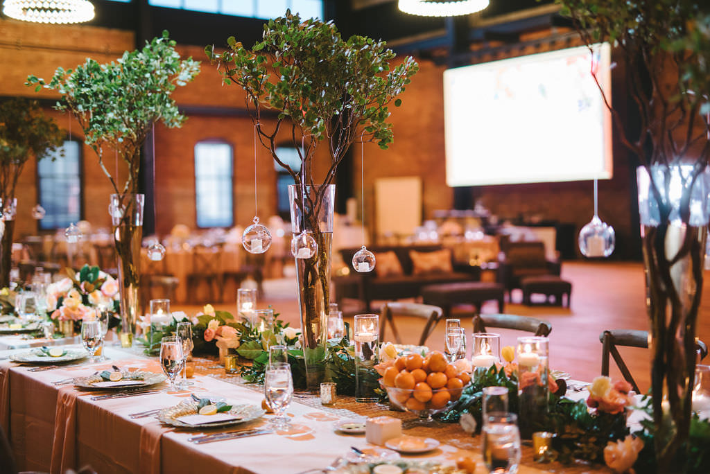 Florida Inspired Wedding Reception Decor, Long Tables with Greenery Garland and Oranges, Wood Chiavari Chairs, Tall Glass Vases with Green Trees and Hanging Glass Cylinder Candles | Tampa Bay Wedding Photographer Kera Photography | Industrial Unique Wedding Venue Armature Works | Wedding Planner Burlap to Lace