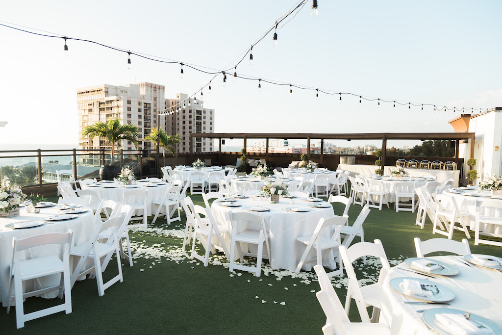 Rustic, Romantic Beach Inspired Rooftop Waterfront Wedding Reception Decor, Round Tables with White Tablecloths, White Folding Chairs, Hanging Bistro Lights, and Low Floral Centerpieces | St. Pete Beach Wedding Venue Hotel Zamora