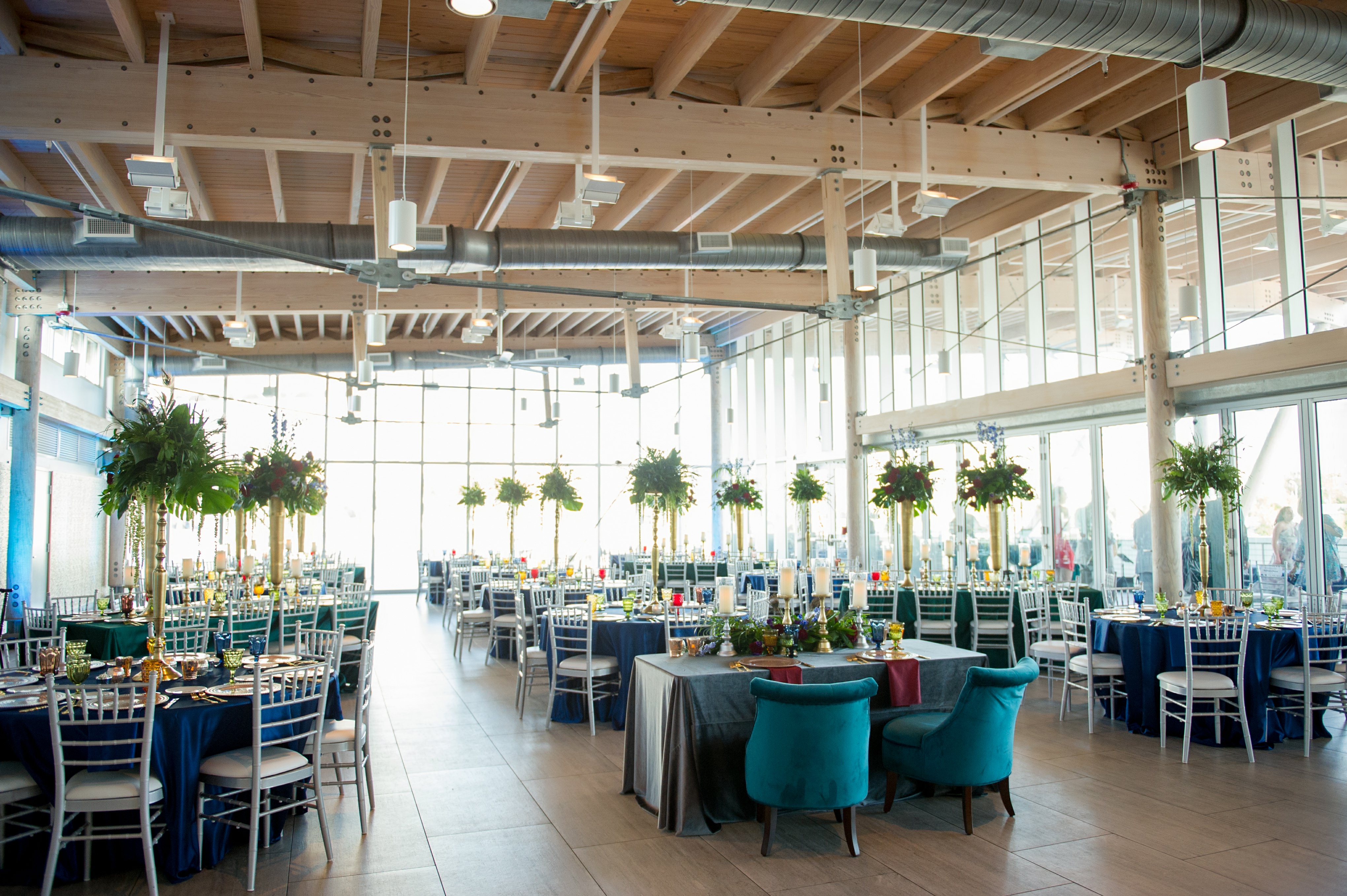 Elegant, Whimsical Eclectic Jewel Toned Themed Reception Wedding Decor at Downtown Tampa Waterfront Reception Venue Tampa Riverwalk, Floor to Ceiling Windows, Large Gold Vase Centerpieces with Overflowing Green Floral Arrangement | Navy Blue Tablecloths with Silver Chairs | Green Velvet Chairs for Sweetheart Table | Tampa Bay Wedding Photographer Andi Diamond Photography