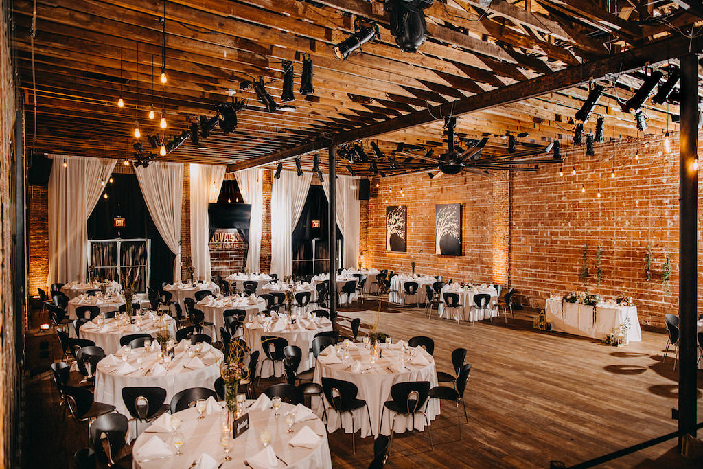 Elegant Tampa Bay Wedding Reception with Romantic Indoor Lighting, Exposed Wood Beams, Red Brick Exposed Wall, White Round Dining Tables with Romantic Wedding Decor, White Sweetheart Table | St. Pete Wedding Venue NOVA 535