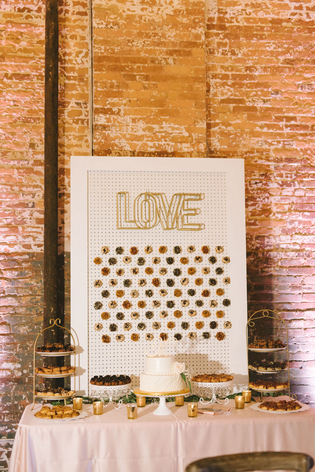 Fun Wedding Dessert Table with Blush Pink Linen, White Display Board with Mini Donut Wall, Gold Love Sign, Two Tier White Wedding Cake | Photographer Kera Photography | Tampa Industrial Wedding Venue Armature Works | Planner Kelly Kennedy Weddings and Events