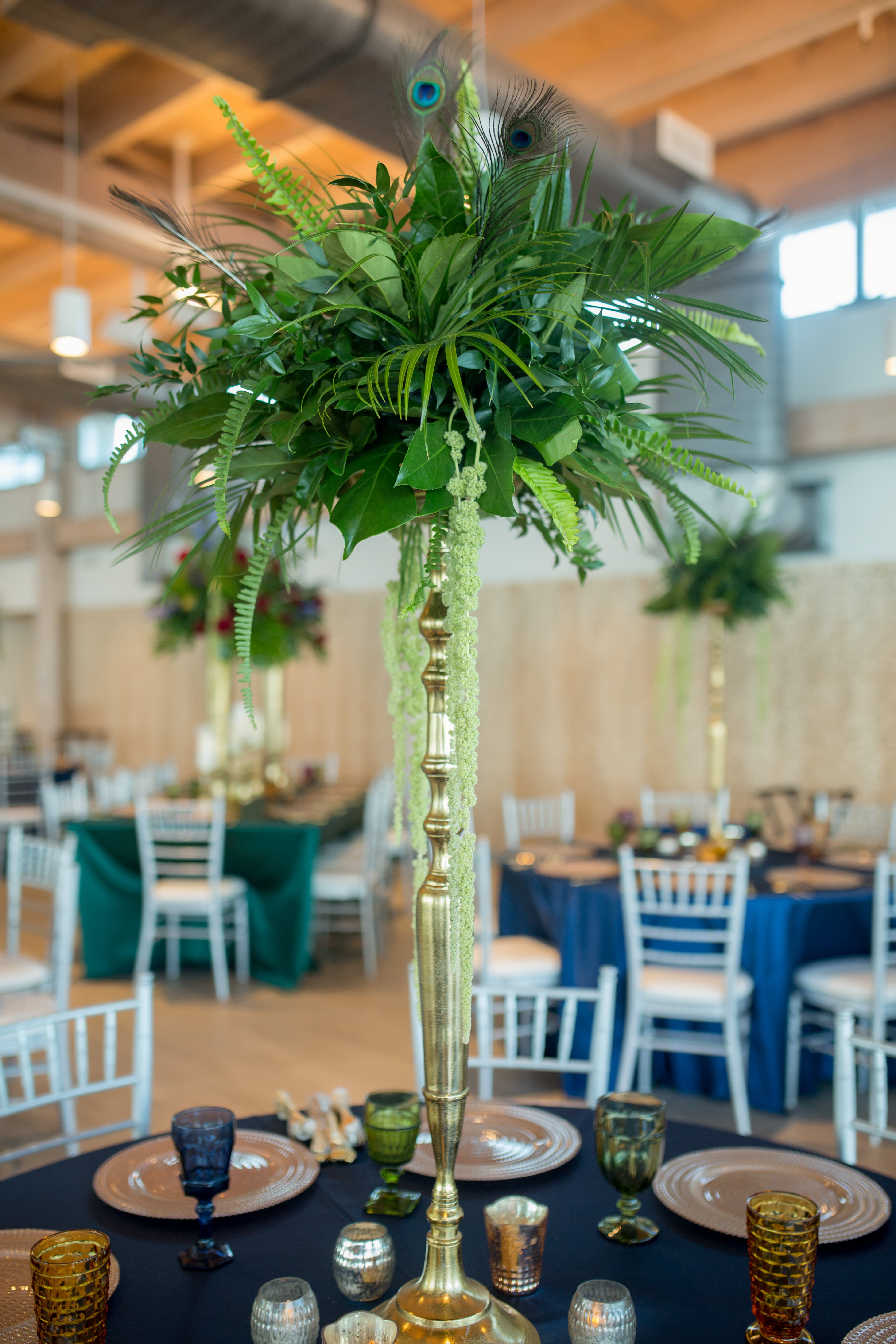 Elegant and Eclectic Jewel Toned Themed Reception Wedding Decor at Tampa River Center, Large Gold Vase Centerpieces with Overflowing Green Floral and Peacock Feather Arrangements | Jewel Tone Tablecloths, Vintage Multi-colored Glass Goblets, Gold Chargers, Tall Silver Candelabras | Tampa Bay Wedding Photographer Andi Diamond Photography