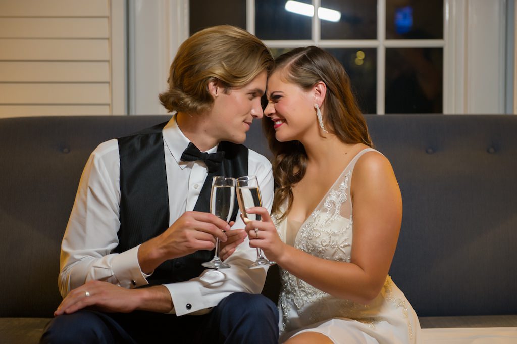 Bride and Groom Toast with Champagne Flutes During Wedding Reception, Bride in Second Look Reception Outfit Streamline White Gown with Embroidered Top and Plunging Neckline | Tampa Wedding Dress Shop Truly Forever Bridal | Tampa Bay Wedding Photographer Andi Diamond Photography
