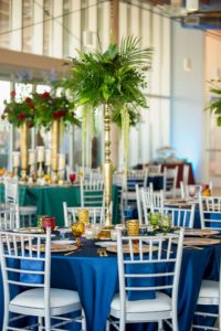 Eclectic Jewel Toned Themed Reception Wedding Decor at Tampa River Center, Large Gold Vase Centerpieces with Overflowing Green Floral Arrangements | Jewel Tone Tablecloths, Vintage Multi-colored Glass Goblets, Gold Flatware, | Tampa Bay Wedding Photographer Andi Diamond Photography