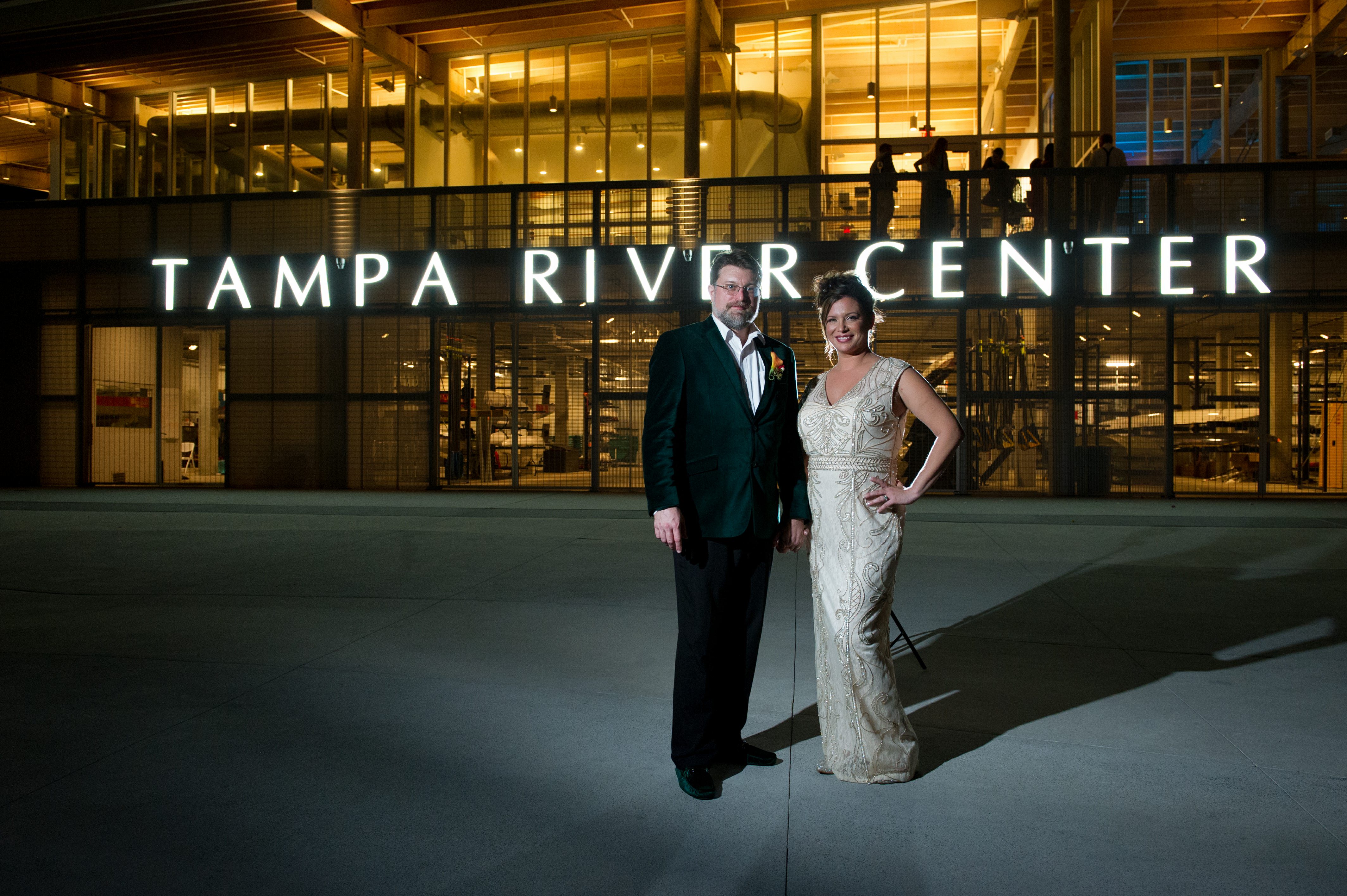 Tampa Bay Bride and Groom in Nighttime Wedding Portrait In Front of Exterior of Tampa River Center in Downtown Tampa at Night, Bride in Ivory Wedding Dress with Gold Detailing, Groom in Emerald Green Velvet Jacket | Tampa Bay Wedding Photographer Andi Diamond Photography| Tampa Bay Wedding Makeup Artist Michelle Renee the Studio