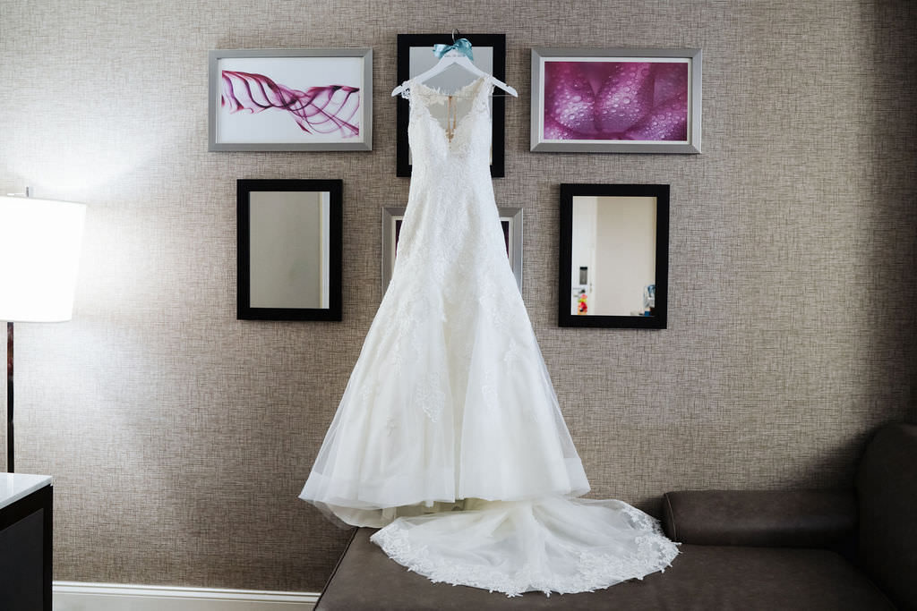 Stella York Lace Fit and flare Lace Overlay Wedding Dress With Low Neckline and Fitted Bodice and Tulle Full Skirt, Hanging on Hanger against Hotel Art Backdrop | Photographer Grind & Press Photography