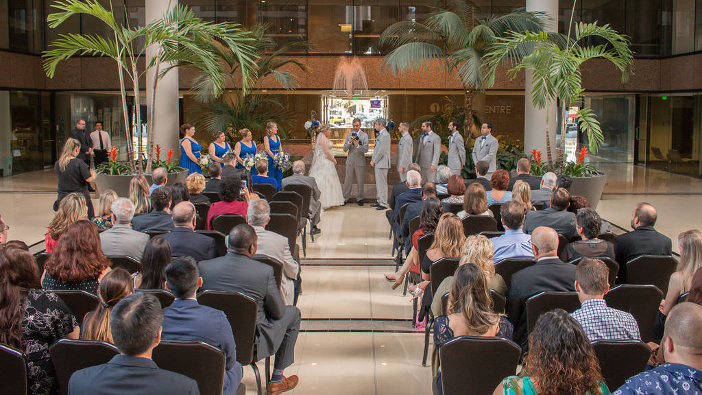 Elegant Indoor Florida Wedding Ceremony, Florida Bride and Groom at Altar, Bridesmaids in Bold Blue, Groomsmen in Light Gray Tuxedos, Palm Tree and Plant Ceremony Decor, Waterfall Fountain in Ceremony Backdrop | Tampa Bay Wedding Venue Tampa Centre Club