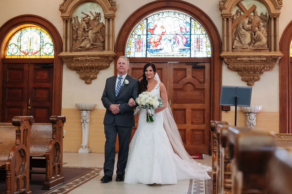 Bride and Father of the Bride Walking Down The Aisle During Wedding Processional at Sacred Heart Catholic Church Tampa, Bride in Stella York Lace Overlay Fit and Flare Wedding Dres, Carrying White and Ivory Rose Bouquet | Photographer Grind & Press Photography