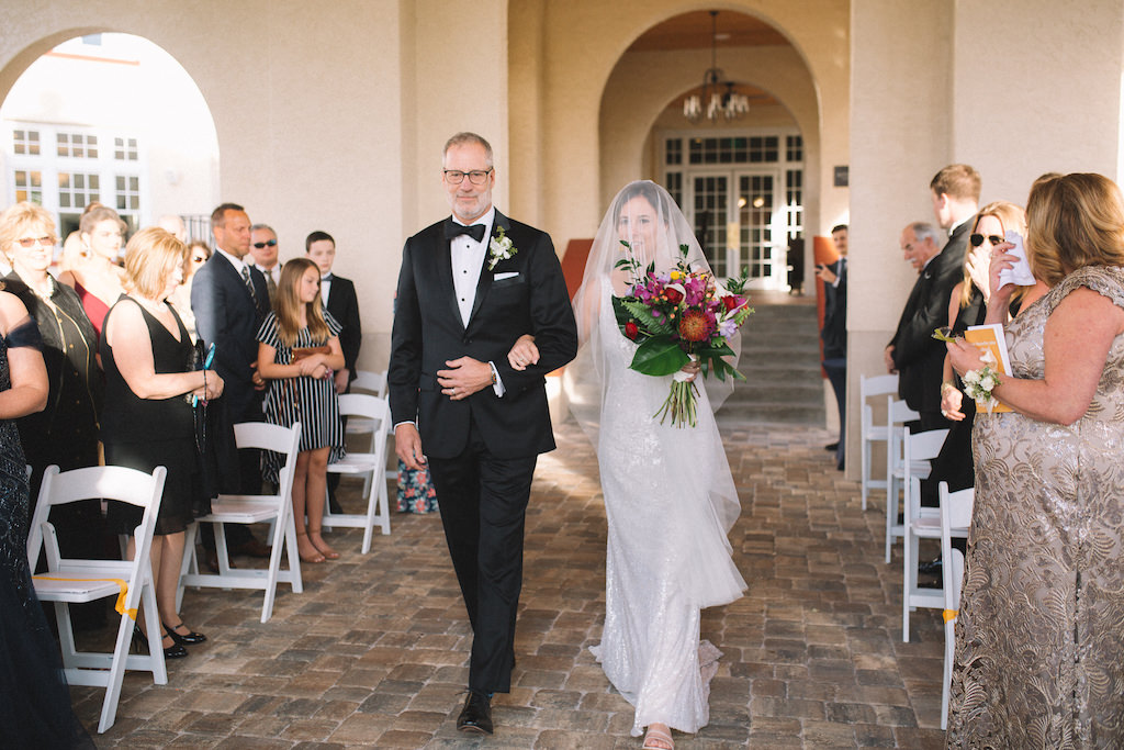 Bride and Father of the Bride Walk Down the Aisle During Wedding Processional, Bride Wearing Sleeveless Sequin Wedding Dress with Tulle Veil, Carrying Tropical Inspired Wedding Bouquet with Colorful Florals and Greenery | Boutique Dunedin Hotel Wedding Venue Fenway Hotel