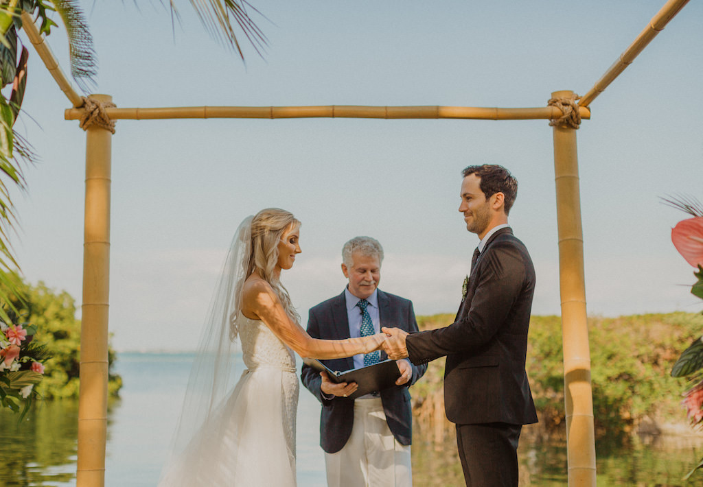 Florida Bride and Groom Exchange Vows under Bamboo Arch in Waterfront Ceremony Photo, Bride in White Spaghetti Strap Beaded Karen Willis Holmes Wedding Dress with Veil | Sarasota Waterfront Wedding Venue Longboat Key Club