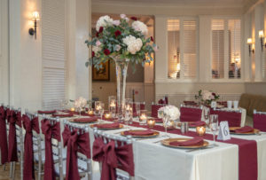 FSU Inspired Elegant Wedding Decor, Tall Floral Centerpiece with White Hydrangeas, Blush Pink Roses and Red Carnations with Silver Dollar Eucalyptus Greenery, Silver Chiavari Chairs with Burgundy Linens, Gold Charges, On Long Feasting Table | Brooksville Golf Course Southern Hills Plantation